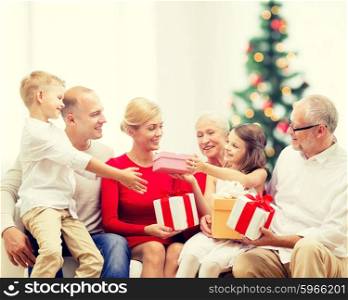family, holidays, generation and people concept - smiling family with gift boxes sitting on couch over living room with christmas tree background