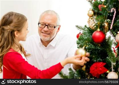family, holidays, generation and people concept - smiling girl with grandfather decorating christmas tree at home