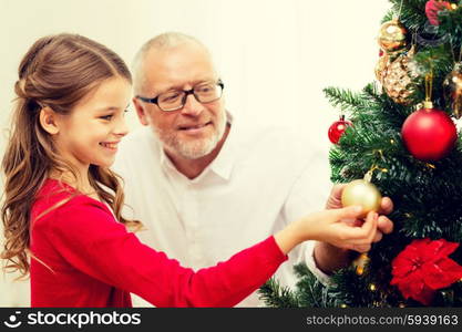 family, holidays, generation and people concept - smiling girl with grandfather decorating christmas tree at home