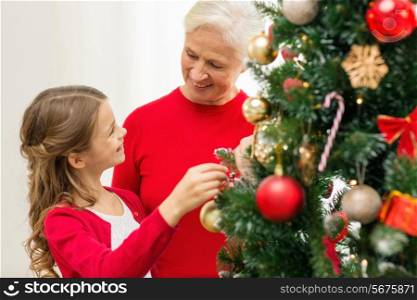 family, holidays, generation and people concept - smiling girl with grandmother decorating christmas tree at home