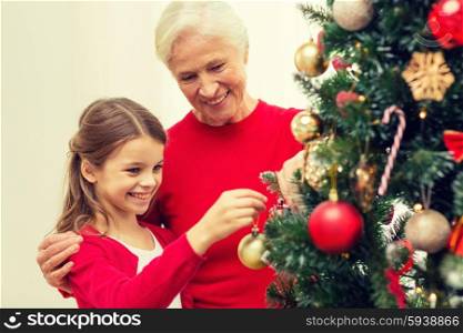 family, holidays, generation and people concept - smiling girl with grandmother decorating christmas tree at home