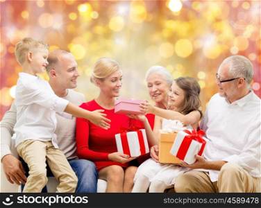 family, holidays, generation, christmas and people concept - happy family with gift boxes sitting on couch over lights background