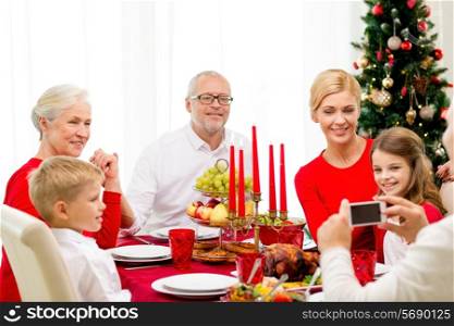 family, holidays, generation, christmas and people concept - smiling family having dinner and making photo with camera at home