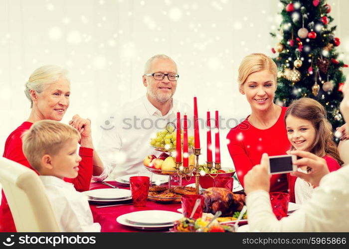 family, holidays, generation, christmas and people concept - smiling family having dinner and making photo with camera at home