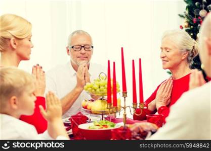 family, holidays, generation, christmas and people concept - smiling family having dinner and praying at home