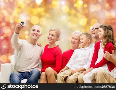 family, holidays, generation, christmas and people concept - smiling family with camera making selfie and sitting on couch over lights background
