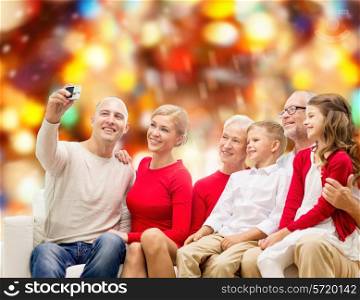 family, holidays, generation, christmas and people concept - smiling family with camera taking selfie and sitting on couch over red lights background