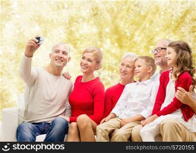 family, holidays, generation, christmas and people concept - smiling family with camera taking selfie and sitting on couch over yellow lights background