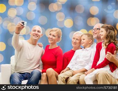 family, holidays, generation, christmas and people concept - smiling family with camera taking selfie and sitting on couch over blue lights background