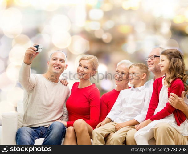 family, holidays, generation, christmas and people concept - smiling family with camera taking selfie and sitting on couch over lights background