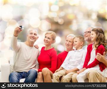 family, holidays, generation, christmas and people concept - smiling family with camera taking selfie and sitting on couch over lights background