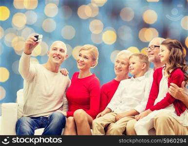 family, holidays, generation, christmas and people concept - smiling family with camera taking selfie and sitting on couch over blue lights background