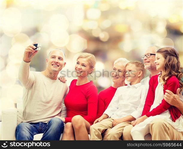 family, holidays, generation, christmas and people concept - smiling family with camera taking selfie and sitting on couch over lights background