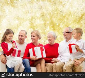 family, holidays, generation, christmas and people concept - smiling family with gift boxes sitting on couch over yellow lights background