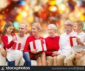 family, holidays, generation, christmas and people concept - smiling family with gift boxes sitting on couch over red lights background