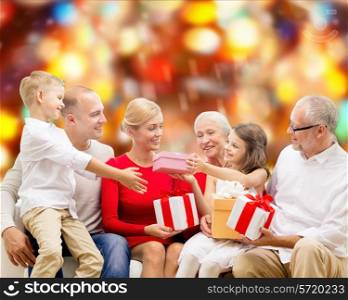 family, holidays, generation, christmas and people concept - smiling family with gift boxes sitting on couch over red lights background