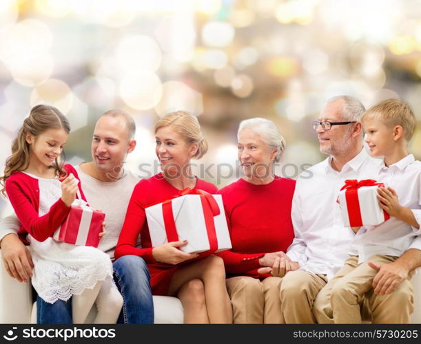 family, holidays, generation, christmas and people concept - smiling family with gift boxes sitting on couch over lights background