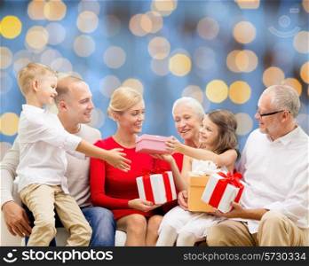 family, holidays, generation, christmas and people concept - smiling family with gift boxes sitting on couch over blue lights background