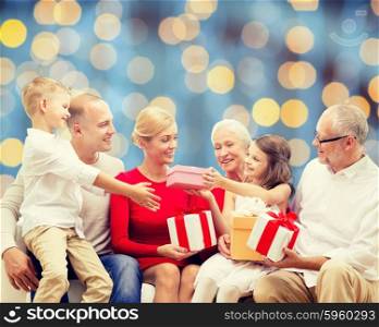family, holidays, generation, christmas and people concept - smiling family with gift boxes sitting on couch over blue lights background