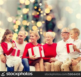 family, holidays, generation, christmas and people concept - smiling family with gift boxes sitting on couch over tree lights background