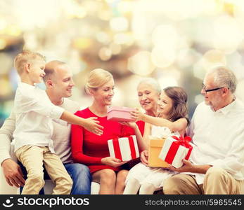 family, holidays, generation, christmas and people concept - smiling family with gift boxes sitting on couch over lights background