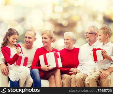 family, holidays, generation, christmas and people concept - smiling family with gift boxes sitting on couch over lights background