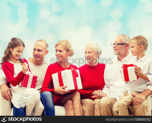 family, holidays, generation, christmas and people concept - smiling family with gift boxes sitting on couch over blue lights background