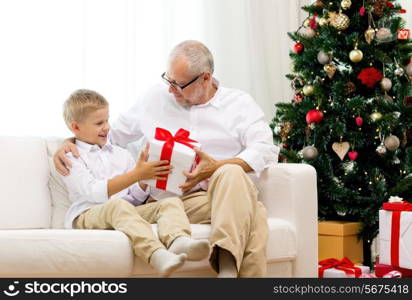 family, holidays, generation, christmas and people concept - smiling grandfather and grandson with gift box sitting on couch at home