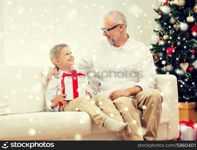 family, holidays, generation, christmas and people concept - smiling grandfather and grandson with gift box sitting on couch at home