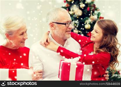 family, holidays, generation, christmas and people concept - smiling grandparents and granddaughter with gift boxes sitting on couch at home