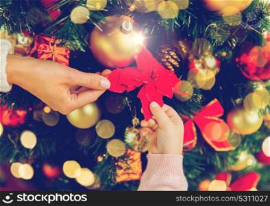 family, holidays, new year and people concept - close up of mother and child hands decorating christmas tree. close up of family decorating christmas tree