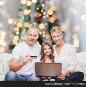 family, holidays, shopping, technology and people concept - happy family with laptop computer and credit card over christmas lights tree background