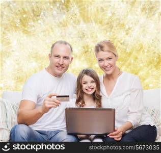 family, holidays, shopping, technology and people concept - happy family with laptop computer and credit card over yellow lights background