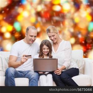 family, holidays, shopping, technology and people concept - happy family with laptop computer and credit card over red lights background