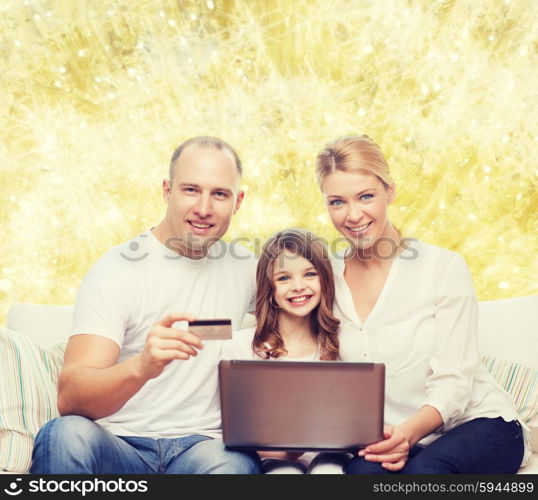 family, holidays, shopping, technology and people concept - happy family with laptop computer and credit card over yellow lights background