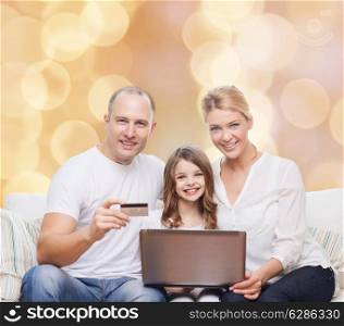 family, holidays, shopping, technology and people concept - happy family with laptop computer and credit card over beige lights background
