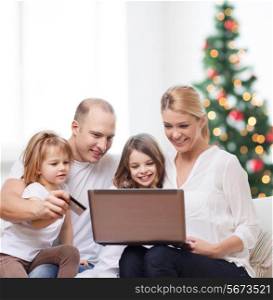 family, holidays, shopping, technology and people - happy family with laptop computer and credit card over living room and christmas tree background