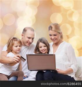family, holidays, shopping, technology and people - happy family with laptop computer and credit card over beige lights background