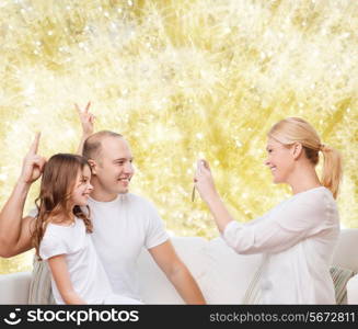 family, holidays, technology and people concept - smiling mother, father and little girl with camera over yellow lights background