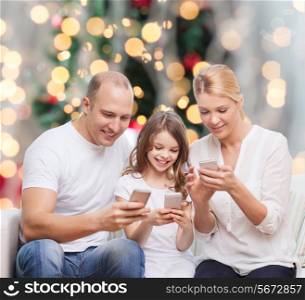 family, holidays, technology and people concept - smiling mother, father and little girl with smartphones over living room and christmas tree background
