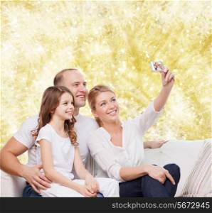 family, holidays, technology and people concept - smiling mother, father and little girl making selfie with camera over yellow lights background