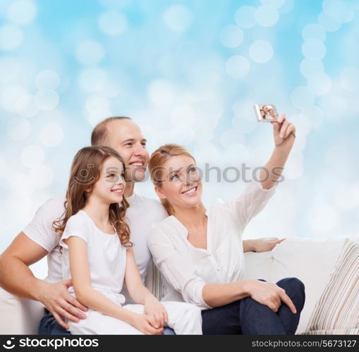 family, holidays, technology and people concept - smiling mother, father and little girl making selfie with camera over blue lights background