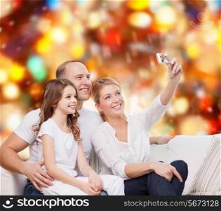 family, holidays, technology and people concept - smiling mother, father and little girl making selfie with camera over red lights background