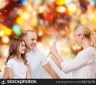 family, holidays, technology and people concept - smiling mother, father and little girl with camera over red lights background