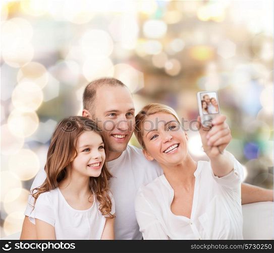 family, holidays, technology and people concept - smiling mother, father and little girl making selfie with camera over lights background
