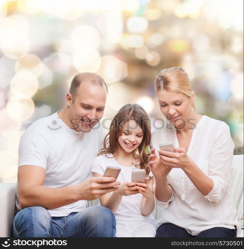 family, holidays, technology and people concept - smiling mother, father and little girl with smartphones over lights background