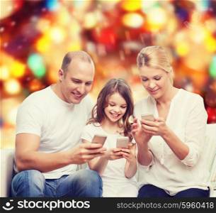 family, holidays, technology and people concept - smiling mother, father and little girl with smartphones over red lights background
