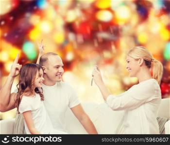 family, holidays, technology and people concept - smiling mother, father and little girl with camera over red lights background