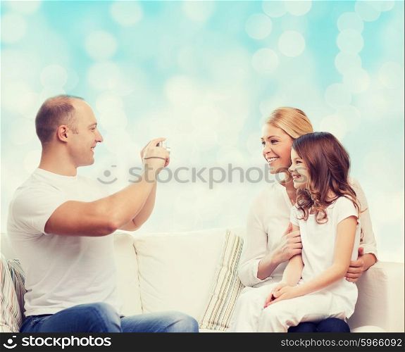 family, holidays, technology and people concept - smiling mother, father and little girl with camera over blue lights background