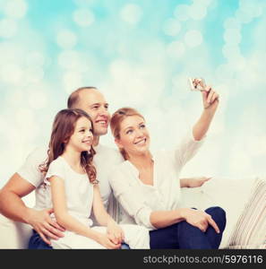 family, holidays, technology and people concept - smiling mother, father and little girl making selfie with camera over blue lights background